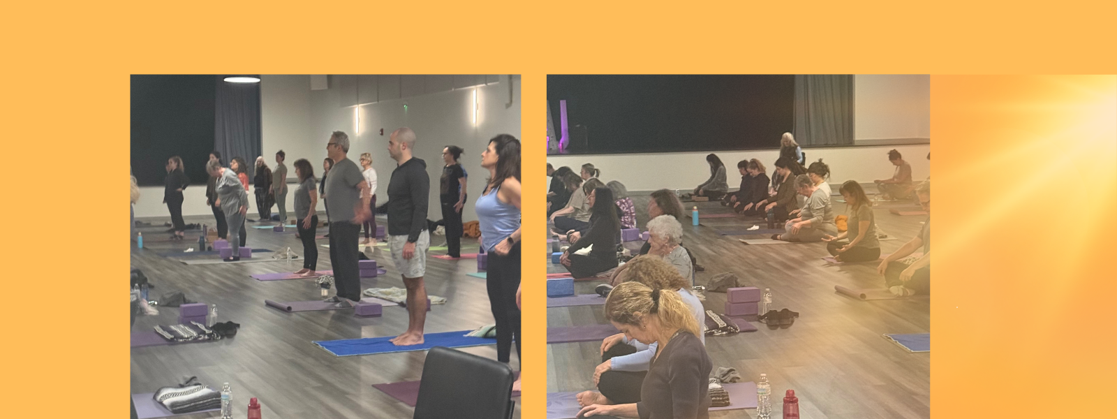 A group of people in an indoor studio participate in a yoga class, standing or sitting on mats while facing the instructor. The room is well-lit, and yoga props are placed on the floor near participants.