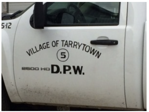 White truck door with "Village of Tarrytown 5" and "2600 HD D.P.W." text in black. The door is slightly dirty, suggesting frequent use.