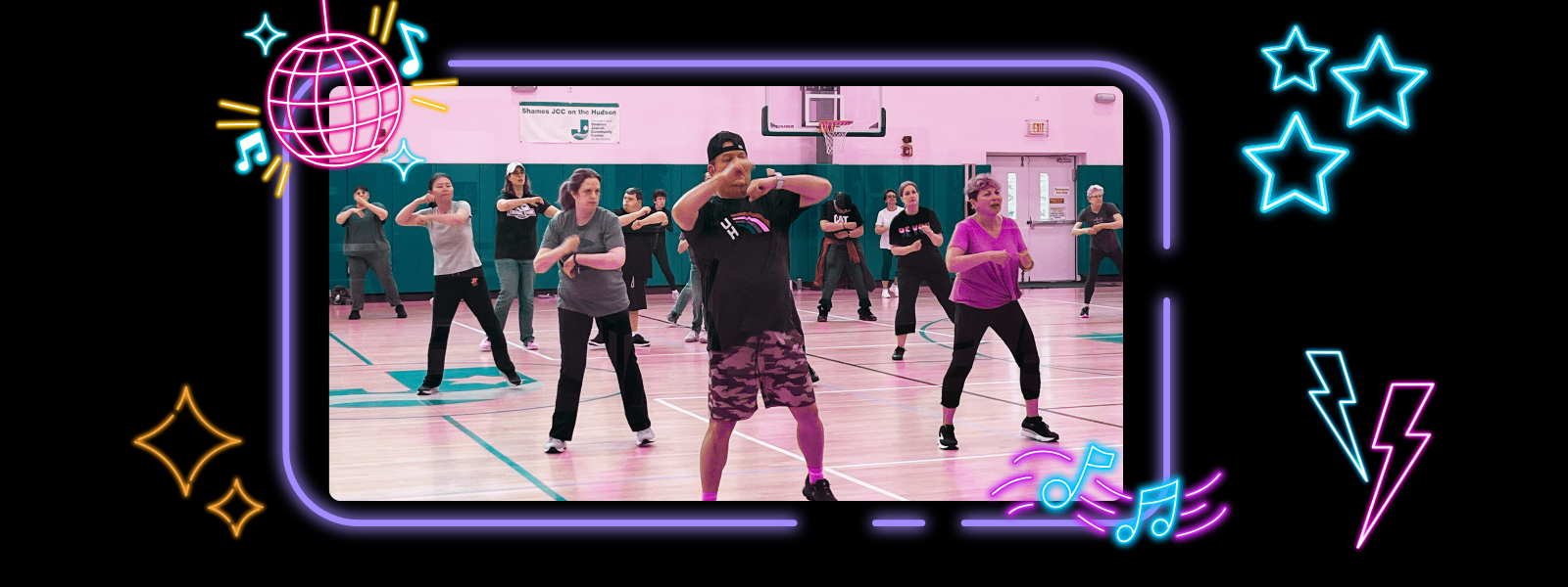 A diverse group of people participates in a lively dance class in a gym, guided by an energetic instructor. Neon decorations add a fun, vibrant mood.