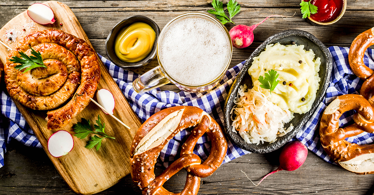 A hearty German meal with pretzels, sausage, mashed potatoes, and sauerkraut on a wooden table. A beer mug, mustard, and radishes are also present.