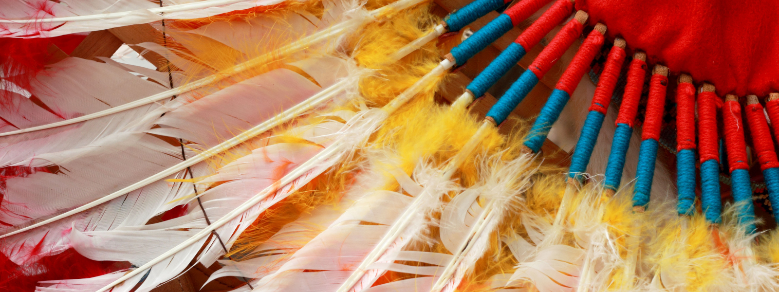 Close-up of a Native American headdress with vibrant red, yellow, and white feathers, adorned with blue and red beads, evoking cultural richness and artistry.