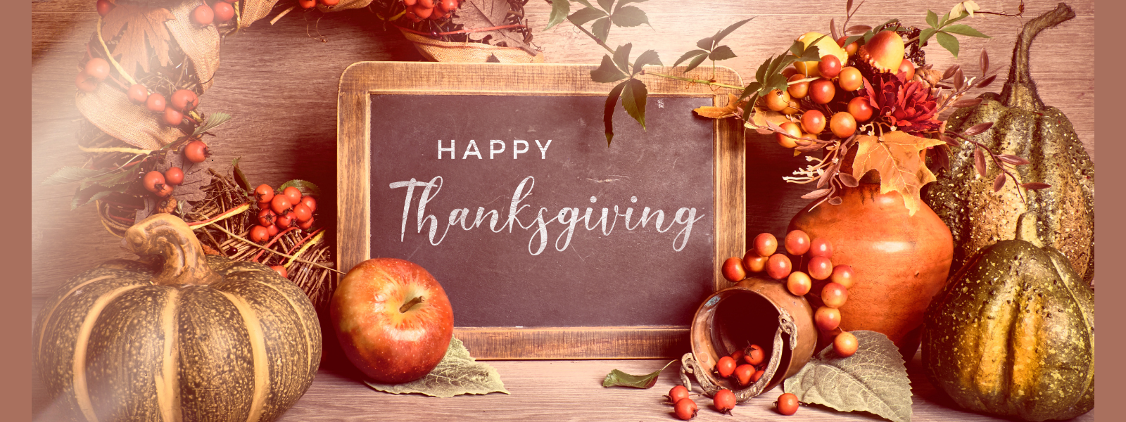 Festive Thanksgiving scene with a chalkboard saying "Happy Thanksgiving" surrounded by autumn leaves, pumpkins, an apple, and berries. Warm, harvest-themed decor.